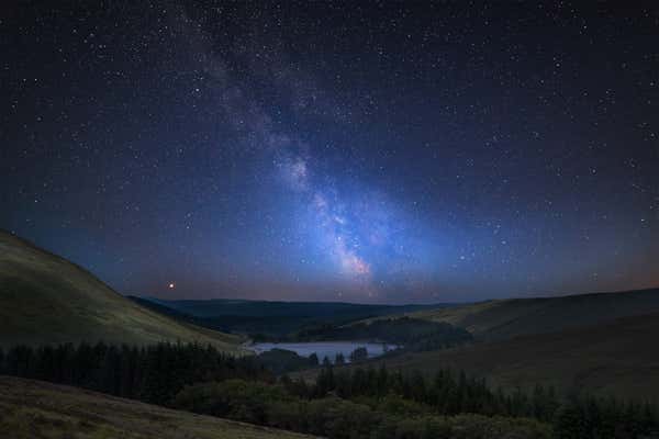 Vibrant Milky Way composite image over landscape of mountains in distance, Brecon Beacons