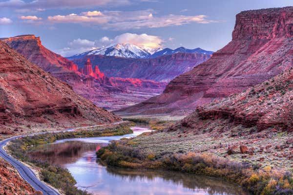 The Colorado River winds its way toward Fisher Towers glowing pink in the late afternoon Autumn light with the snow-capped La Sal Mountains behind near Castle Valey, Utah.