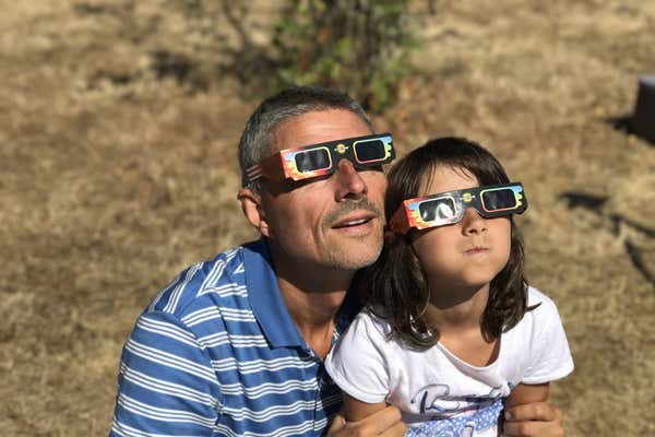 Father and daughter watching a solar eclipse wearing protective glasses