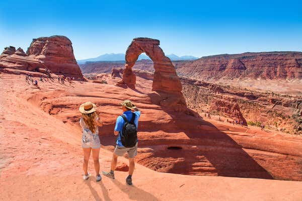 Couple on vacation hiking trip. Man and woman standing on top of the mountain looking at beautiful view. Delicate Arch, Moab, Utah, Arches National Park.